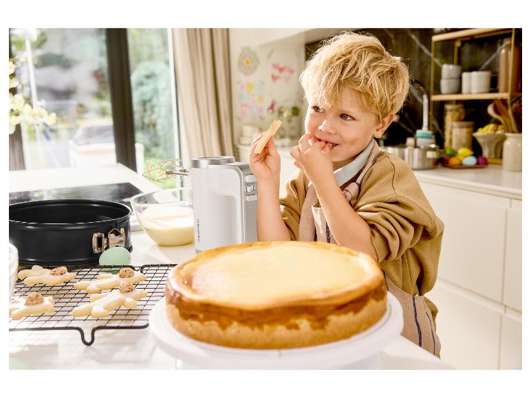 Garçon mangeant un biscuit à côté d'un mixeur Silvercrest et d'un cheesecake dans la cuisine