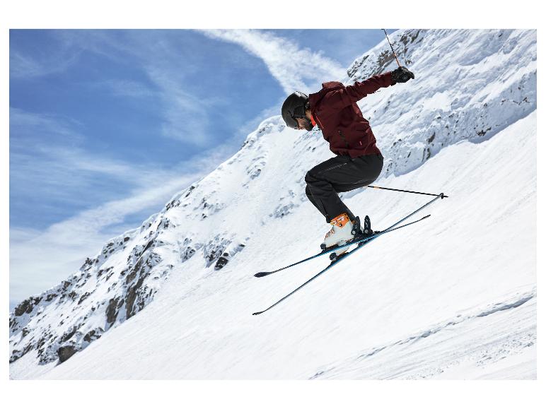 Skieur en veste rouge et pantalon noir sautant sur une piste de ski.