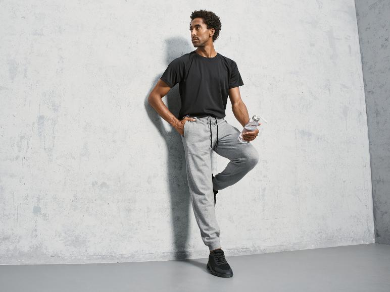 Homme en T-shirt noir et pantalon de survêtement gris avec une bouteille d'eau.