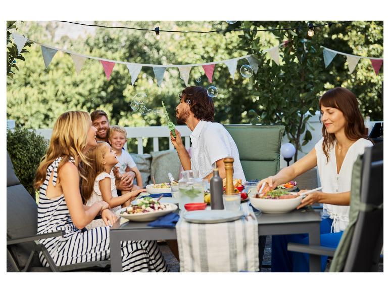 Famille mangeant dehors, bulles de savon et mobilier de jardin.