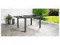 Table de jardin extensible avec plateau en verre sur une terrasse avec plantes.