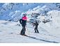 Deux skieurs en tenue de sport d'hiver sur une piste de montagne enneigée avec un village en arrière-plan.