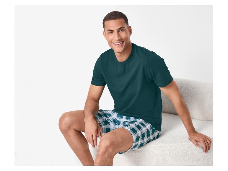Homme souriant en t-shirt vert foncé et short à carreaux, assis sur un canapé.