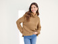 Une femme porte un pull marron à col roulé et un jean bleu.