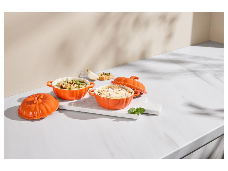 Deux cocottes orange en forme de citrouille avec de la nourriture sur une planche en marbre.