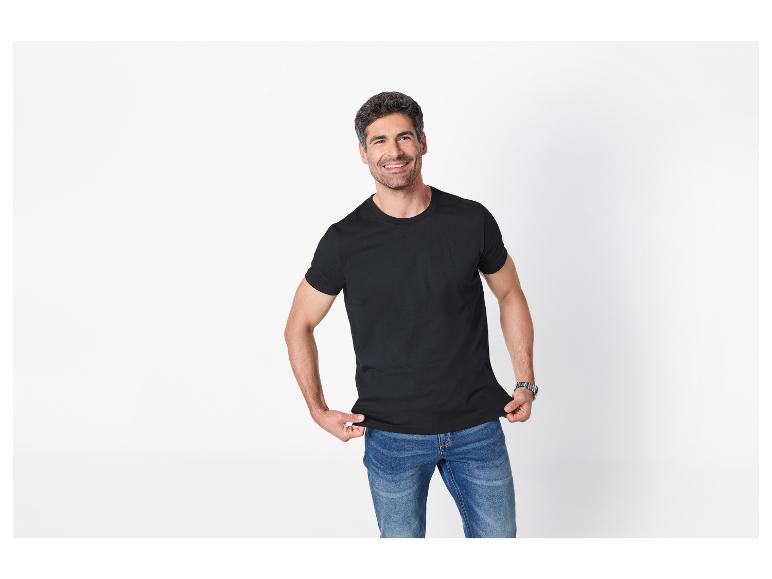 Homme en t-shirt noir et jean bleu, souriant sur fond blanc.
