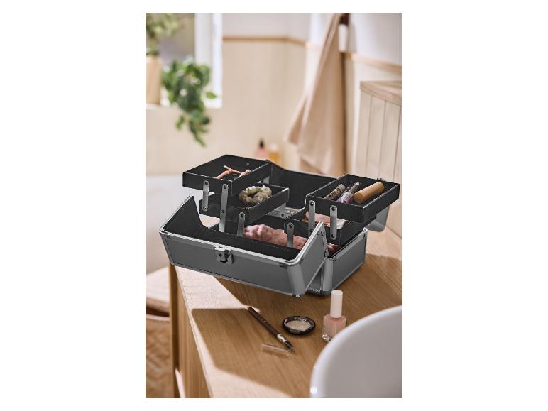 Trousse de maquillage noire ouverte avec cosmétiques et accessoires sur un comptoir en bois.
