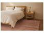 Chambre avec lit en bois clair, linge de lit blanc et tapis rose