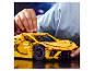Un enfant joue avec une voiture de sport LEGO Technic jaune sur une table sombre.