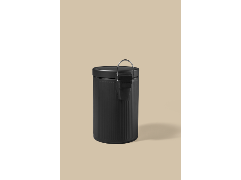 Boîte en métal noir mat avec couvercle à loquet, sur fond beige.