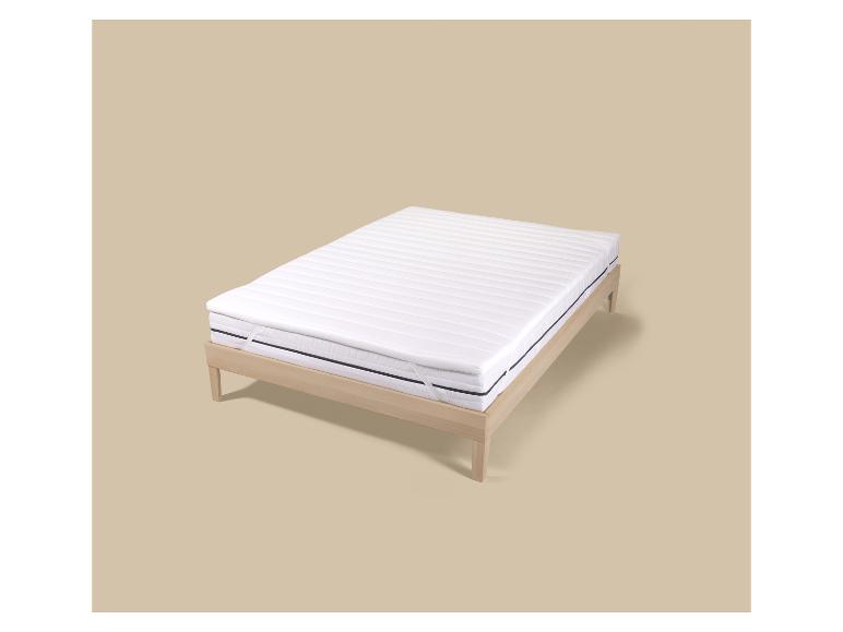 Matelas blanc avec surmatelas et cadre de lit en bois clair sur fond beige.