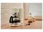 Cafetière crème avec carafe, à côté de café, lait et une tasse sur un comptoir en bois.