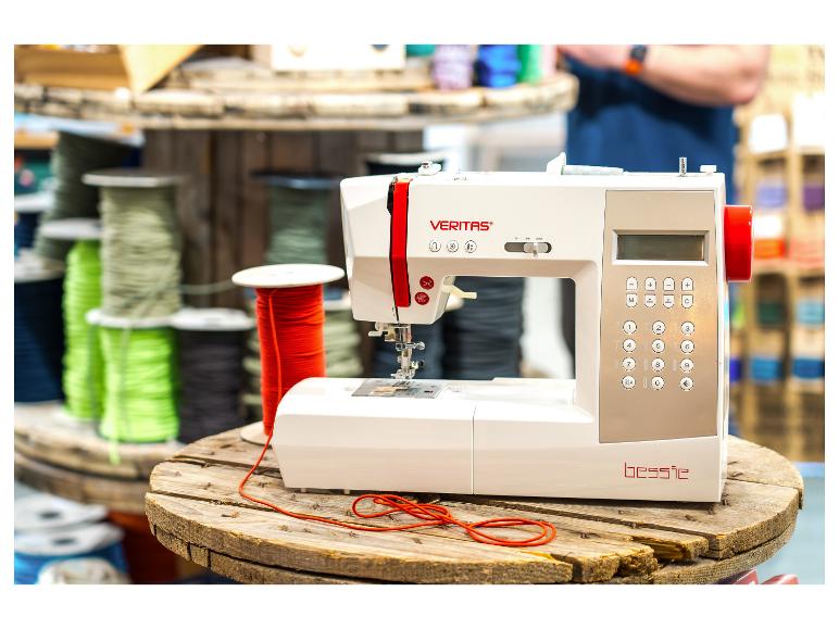 Une machine à coudre blanche avec des accents rouges sur une bobine en bois, entourée de bobines de fil colorées.