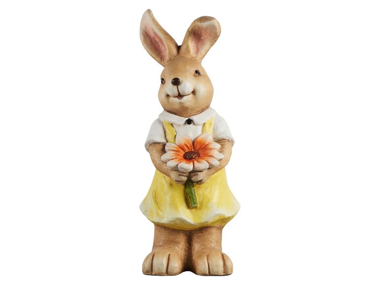 Décoration de Pâques : figurine de lapin souriante en robe jaune tenant une fleur orange.