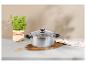 Casserole en acier inoxydable avec couvercle en verre, herbes fraîches et planche en bois sur comptoir en marbre.