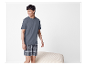 Homme portant un t-shirt gris et un short à carreaux.