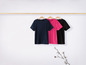 Trois t-shirts, bleu marine, rose et noir, suspendus à une tringle en bois.