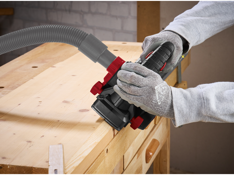 Outil électrique avec aspiration de poussière utilisé sur un établi en bois.