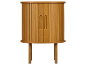 Meuble en bois clair avec portes à tambour et poignées sculptées, sur pieds élancés.