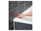 Une main utilisant un outil rouge pour appliquer du mastic autour d'une baignoire blanche.