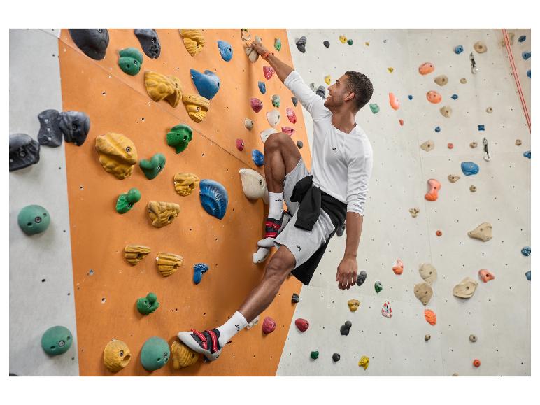 Homme en haut blanc à manches longues et short gris faisant de l'escalade en salle