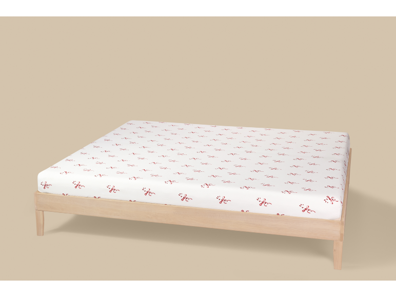 Drap-housse blanc à motif de nœuds rouges sur un cadre de lit en bois clair.