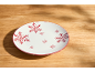 Assiette blanche avec des flocons de neige rouges sur une table en bois.