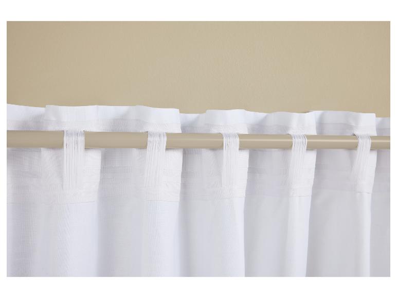 Rideaux blancs à pattes sur une tringle à rideaux marron clair contre un mur beige.