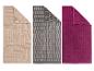 Trois serviettes de bain : beige à motifs géométriques, grise à motifs de briques, et fuchsia unie.
