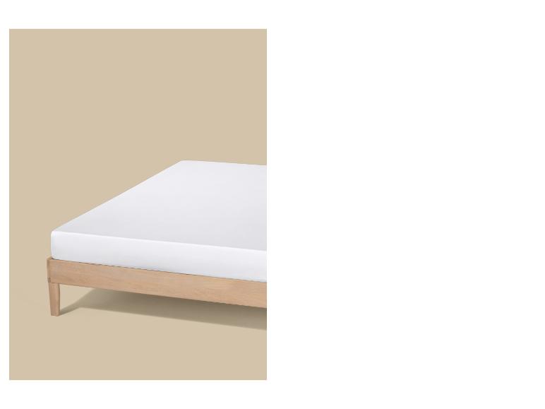 Un matelas blanc sur un cadre de lit en bois clair sur fond beige.