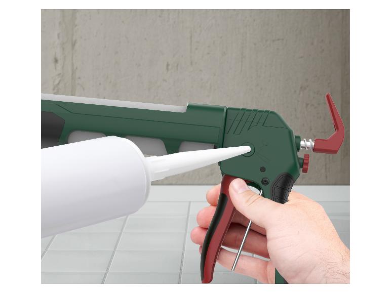 Une main tient un pistolet à calfeutrer vert et rouge avec un tube de mastic blanc inséré.