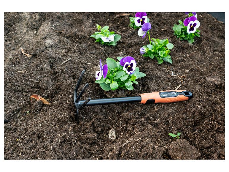 Pensées violettes plantées dans la terre à côté d'un outil de jardinage orange.