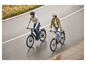 Deux personnes font du vélo électrique sur une route mouillée.