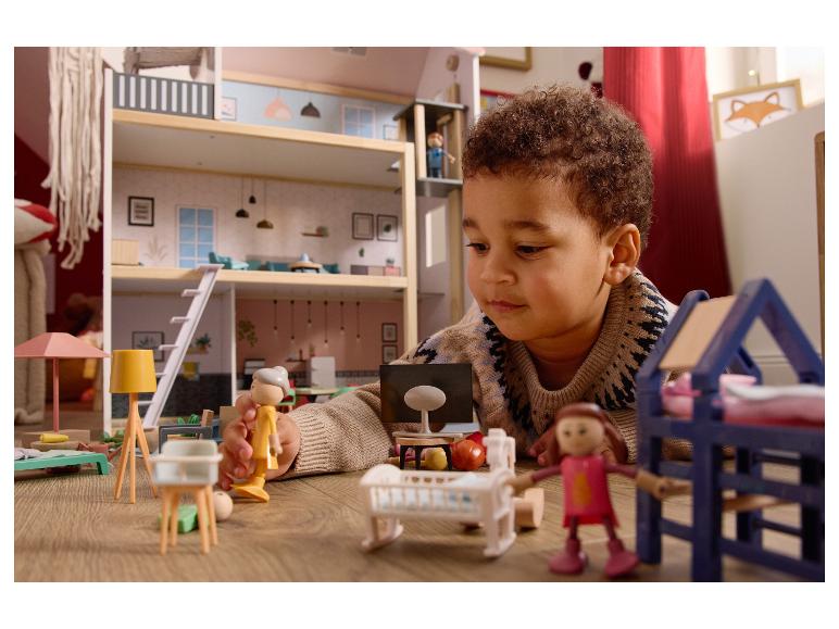 Un enfant joue avec une maison de poupée et de petites figurines sur un parquet.