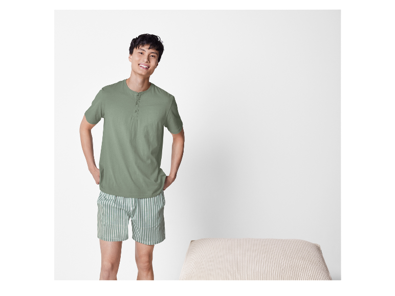 Homme souriant portant un pyjama vert clair à manches courtes et un short rayé.