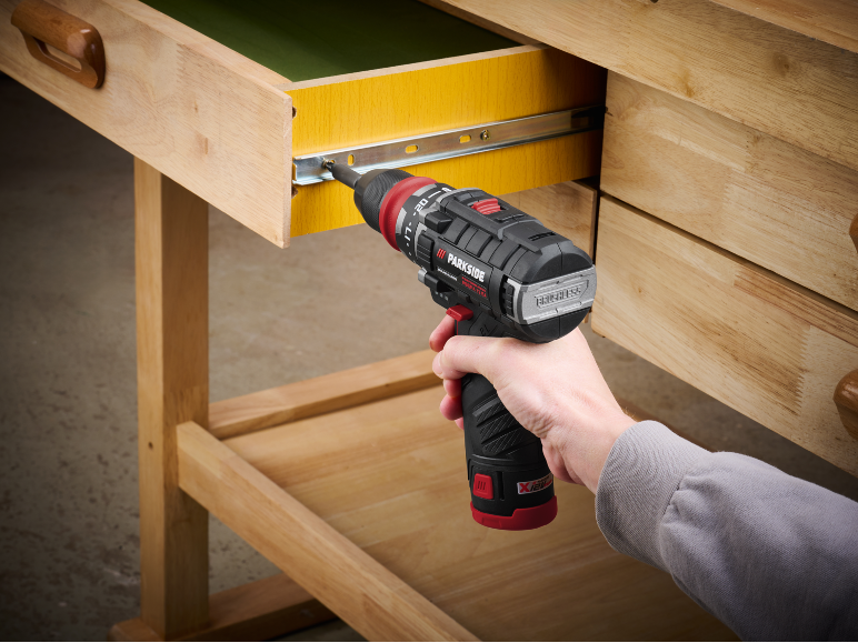 Main utilisant une perceuse sans fil pour installer une glissière de tiroir sur un établi en bois.