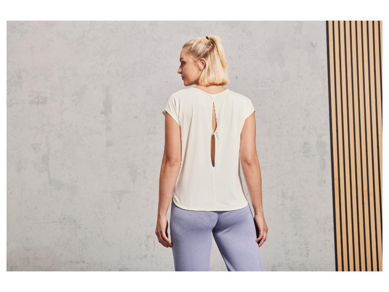Une femme porte un t-shirt blanc avec un dos ouvert et un pantalon bleu clair.