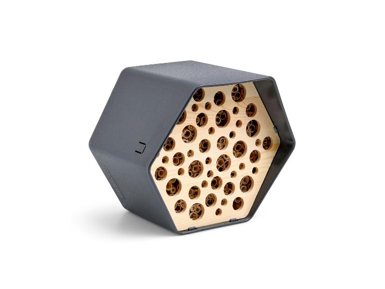Hôtel à insectes hexagonal avec une coque extérieure gris foncé et un intérieur en bois avec des trous de différentes tailles.