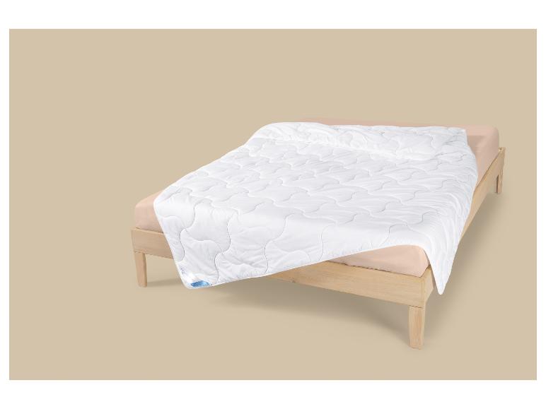 Couette blanche à motif ondulé sur un lit en bois avec des draps beiges