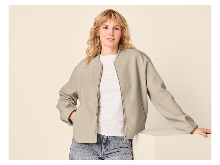 Femme en blouson aviateur gris clair, t-shirt blanc et jean, posant sur fond clair.