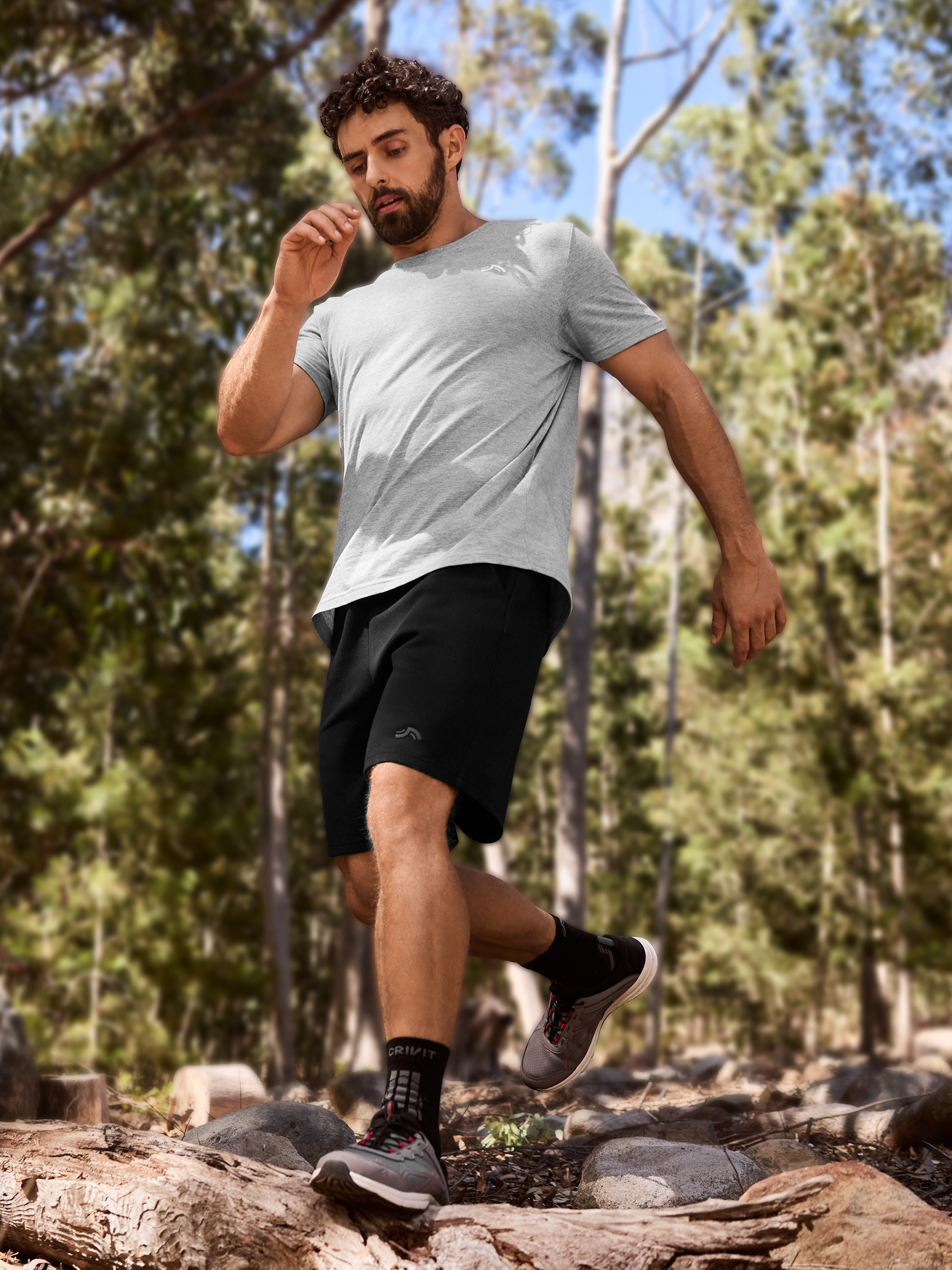 Homme en t-shirt gris et short noir courant sur un sentier forestier.