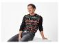 Homme souriant portant un pull de Noël noir avec des motifs festifs et un jean gris.