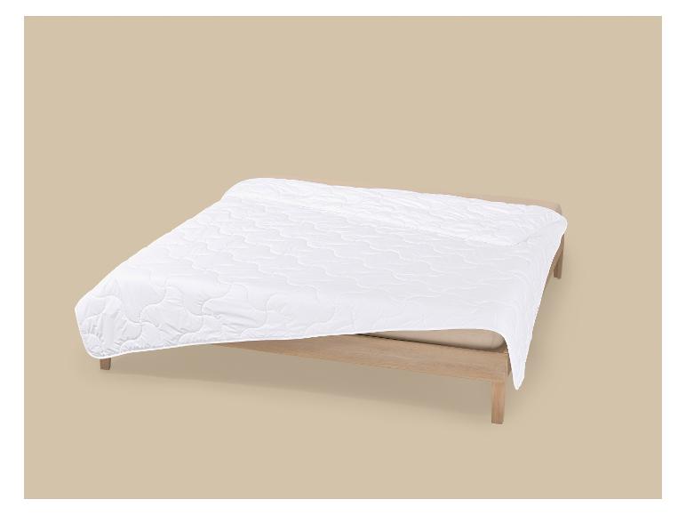Couette blanche matelassée sur un lit en bois avec un fond beige
