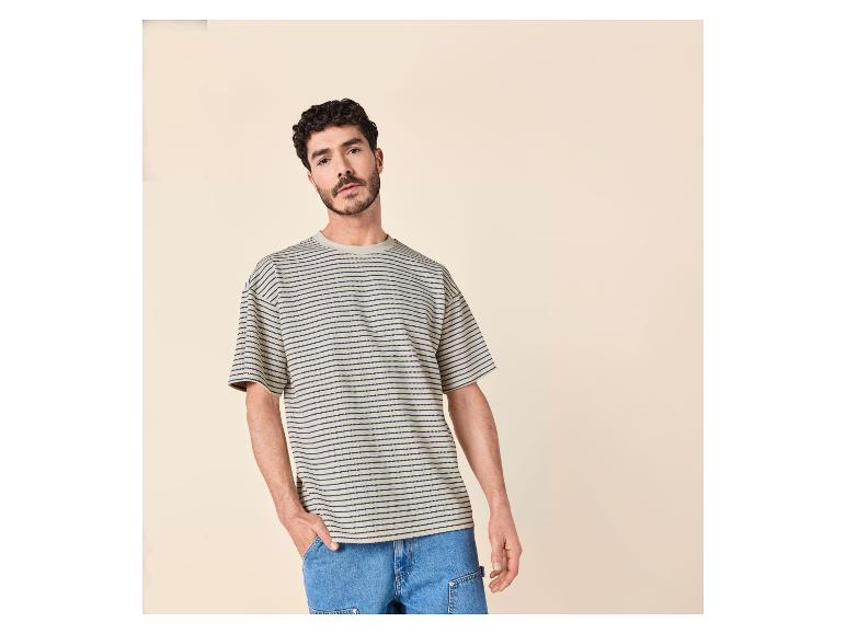 Homme en t-shirt rayé beige et bleu marine, pantalon en jean bleu, main dans la poche.