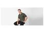 Un homme portant un polo vert et un pantalon noir est assis sur une chaise blanche.