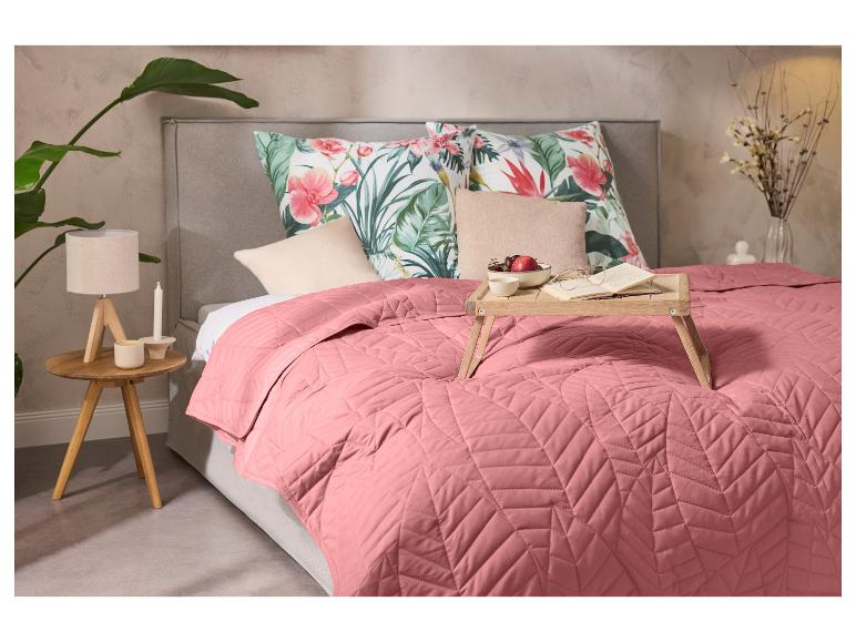 Chambre avec un couvre-lit rose, des oreillers à motifs floraux et un plateau de petit-déjeuner en bois.