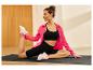 Femme sur un tapis de yoga s'étirant, vêtue de vêtements de sport noirs et d'une veste rose.