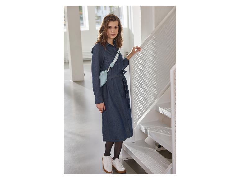 Femme en robe en jean, sac banane bleu clair et baskets blanches près d'un escalier.