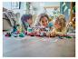 Une mère et deux enfants jouent avec des voitures de course LEGO Duplo colorées sur le sol.