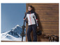Une femme en tenue de ski tenant des skis et un casque devant un mur en bois.